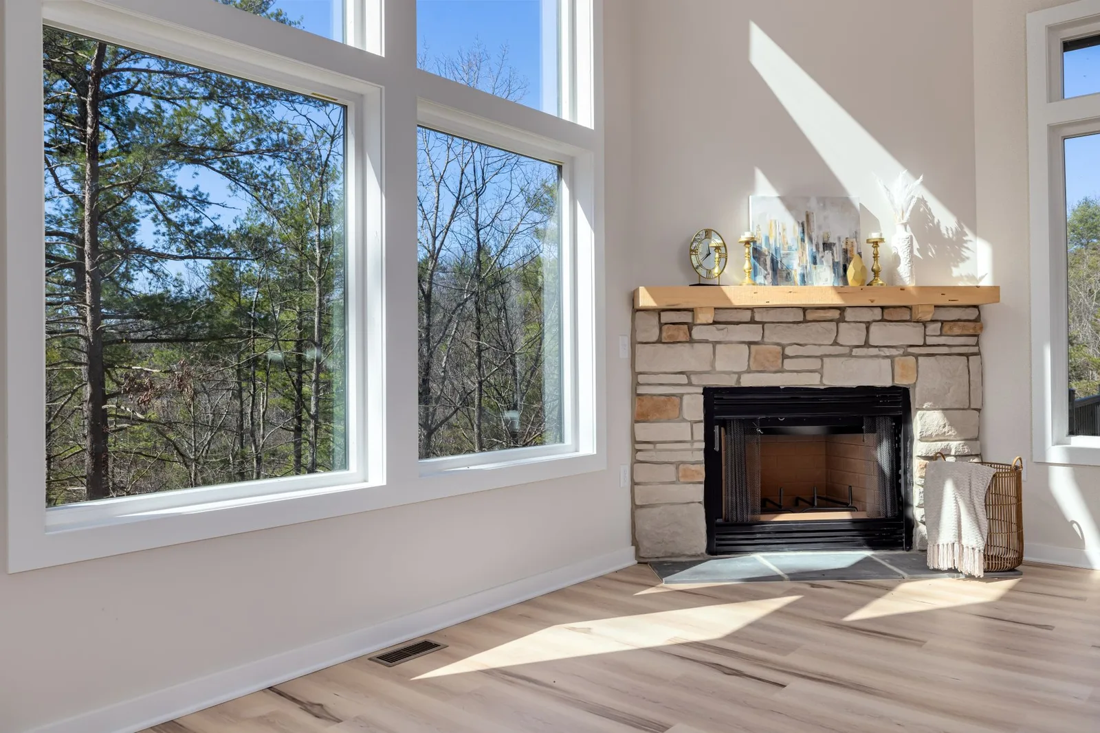 A bright, empty living room with tall windows and a stone fireplace before redesign.