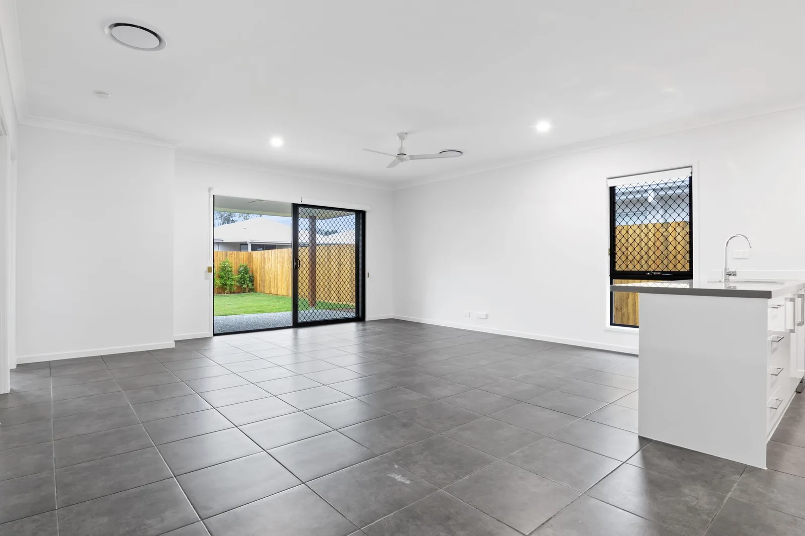 An empty open-plan living and kitchen area with grey tile floors and sliding doors to the yard.